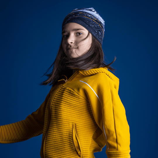 Jeune fille en manteau jaune, tournée dynamiquement, portant la tuque Abracadabra comme bandeau.
