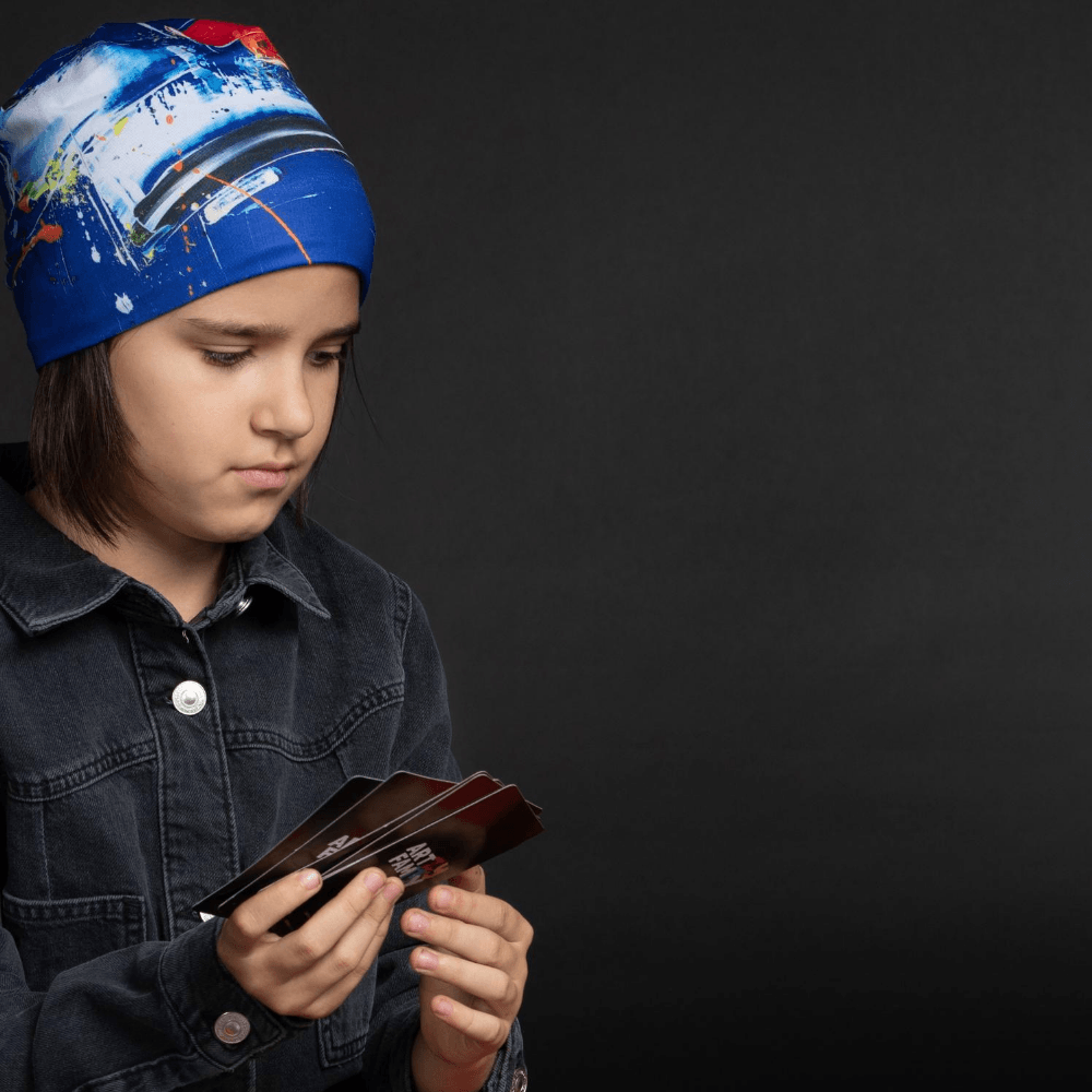 Jeune personne portant la tuque bleue abstraite et une veste en jean, regardant pensivement un jeu de cartes.
