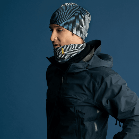 A man wearing a dark winter jacket and a black beanie, with the Abstract Lines multifunctional tube worn as a neck gaiter.