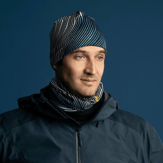 A man wearing a dark winter jacket and a matching beanie, with the Abstract Lines multifunctional tube worn as a neck gaiter, looking to the side.