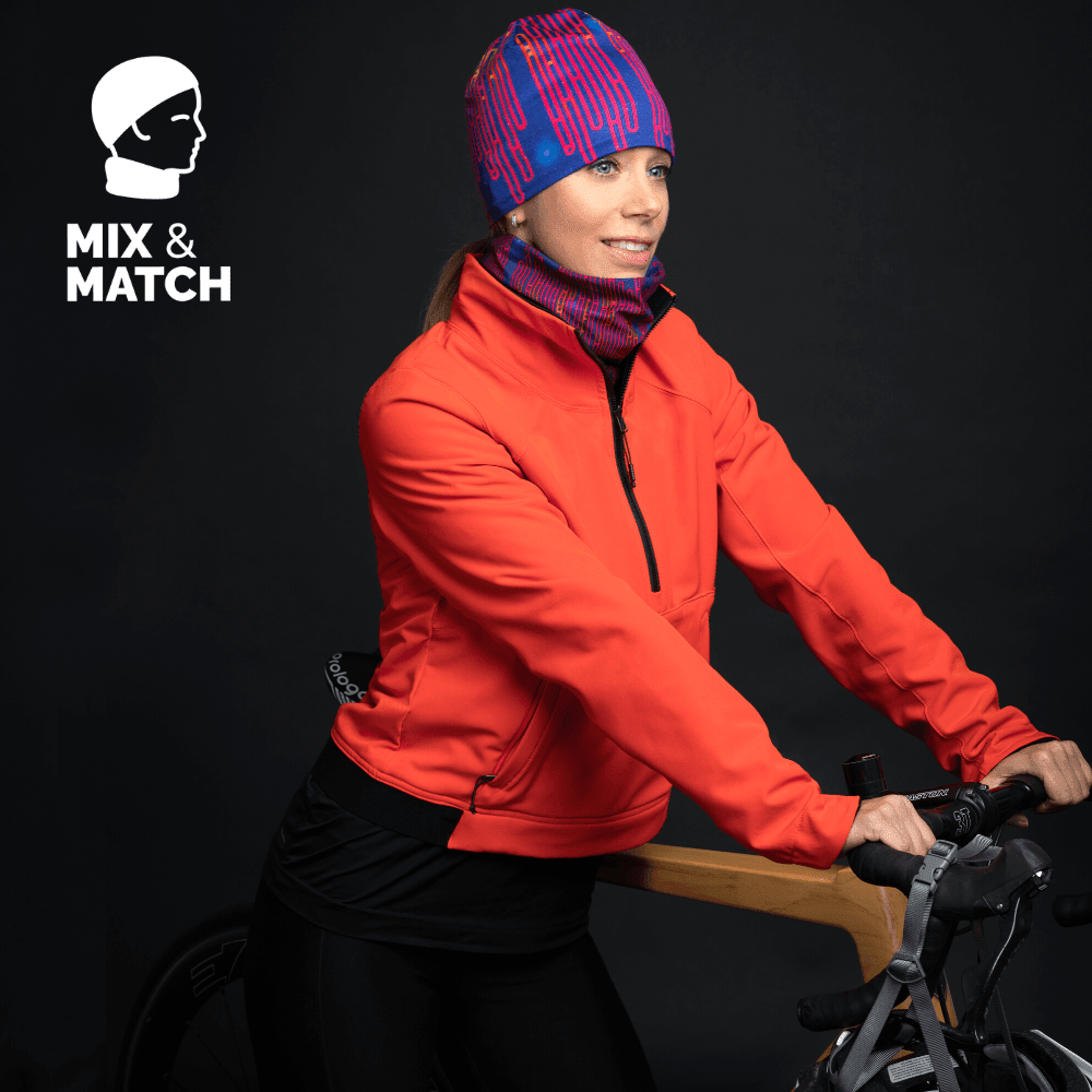 Femme portant une tuque bleue et rose assortie à un cache-cou orange, avec une veste orange, debout à côté d&