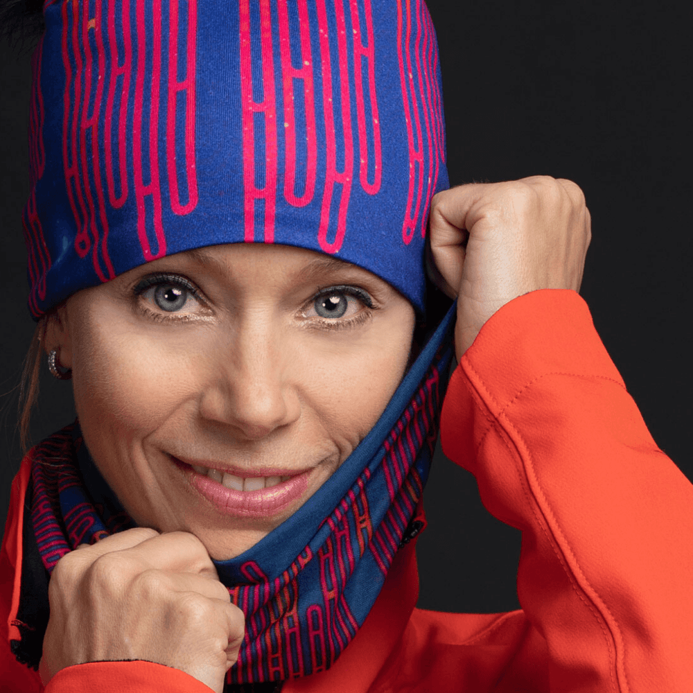 Woman wearing a blue loops beanie and neck tube, pulling the fabric near her face.