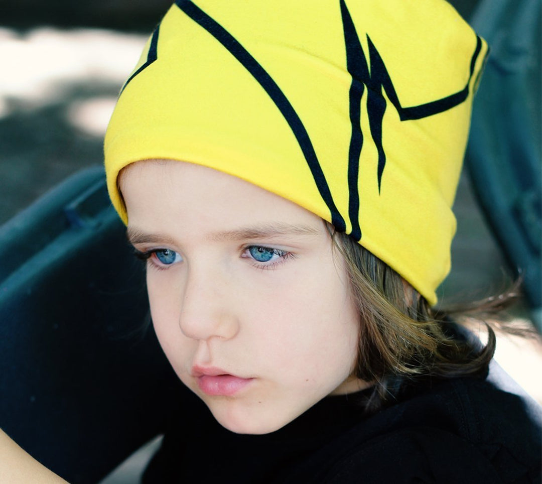 Enfant aux yeux bleu vif portant une tuque jaune avec un motif de lignes noires brisées.