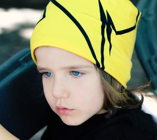 Enfant aux yeux bleu vif portant une tuque jaune avec un motif de lignes noires brisées.