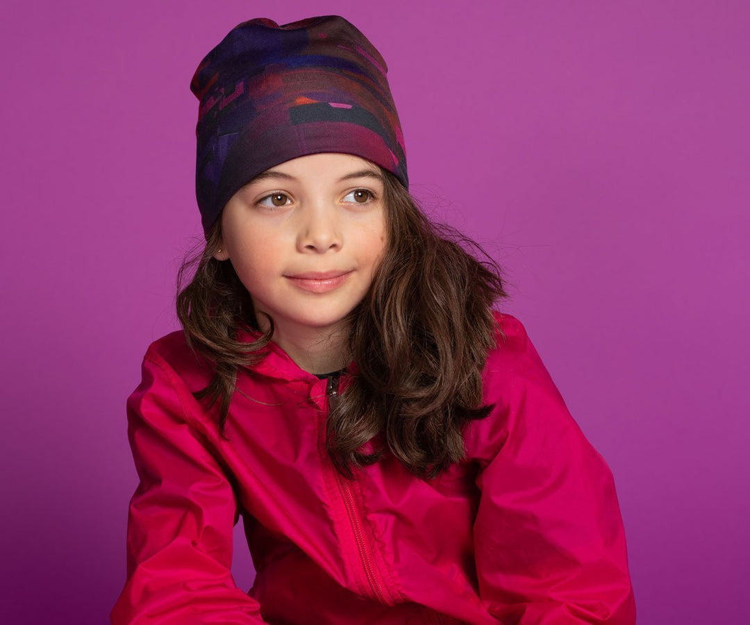 Une jeune fille portant la Tuque Ville, qui affiche un imprimé abstrait vibrant, sur fond violet uni.