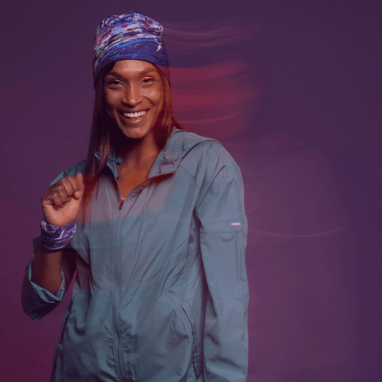 Une femme souriante portant une veste bleue et un bandeau orné du motif artistique Cosmique.