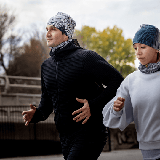 A man and woman wearing matching Dark Steel beanies and neck gaiters while jogging outdoors.