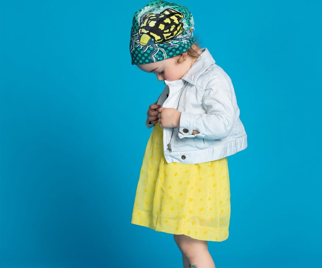 Un jeune enfant portant la tuque Scarabée Plongeur avec une veste claire et une robe jaune, regardant vers le bas.