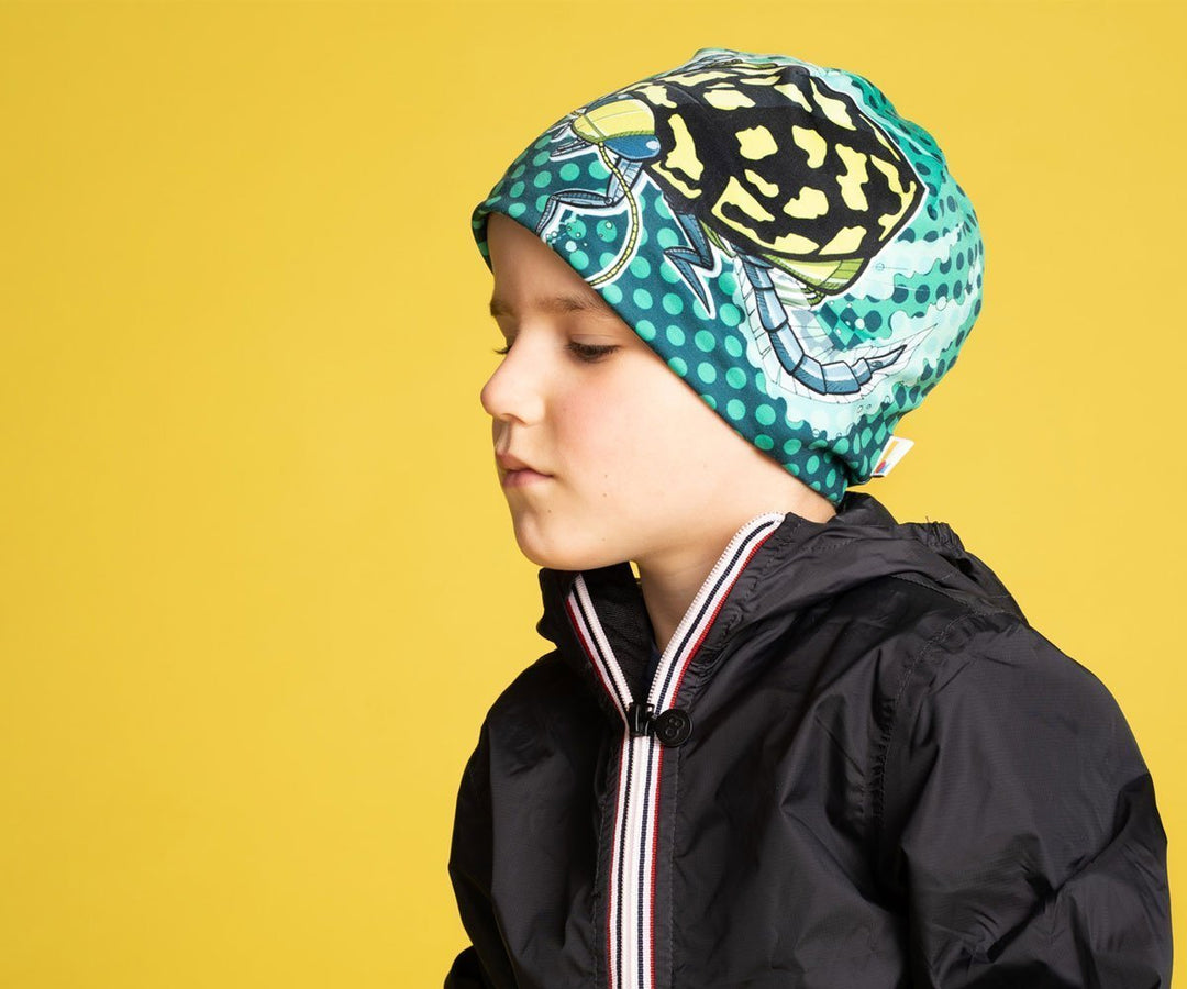 Un enfant portant la tuque Scarabée Plongeur avec une veste noire, regardant pensivement sur le côté.