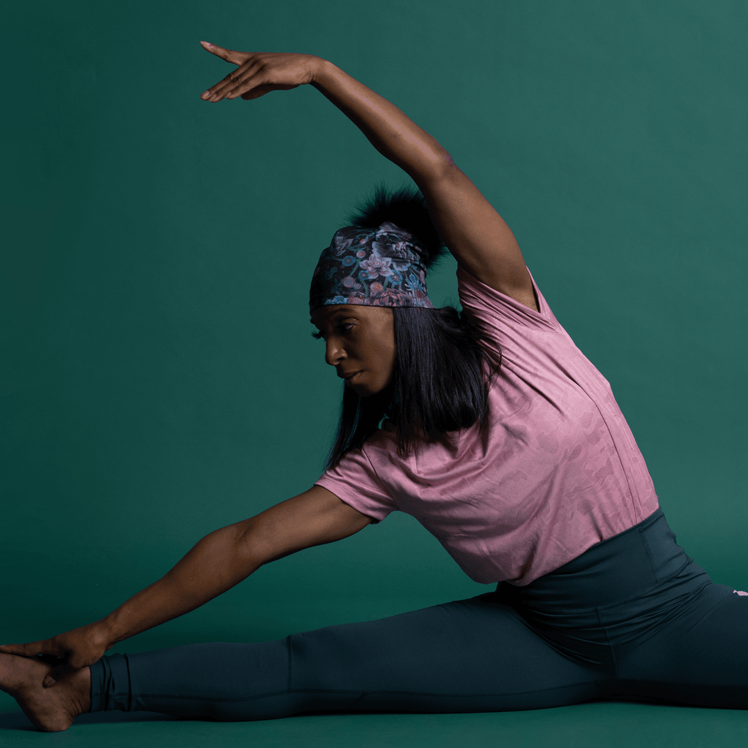 Femme en haut rose et legging sombre exécutant une pose de yoga, portant la Tuque Pompon Flora.
