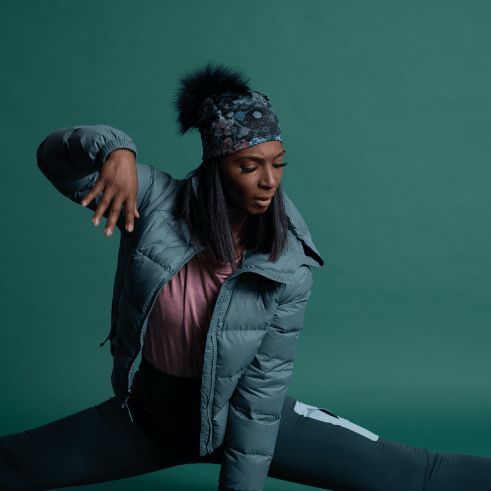 Femme portant la Tuque Pompon Flora et une veste d'hiver grise, en grand écart de yoga.