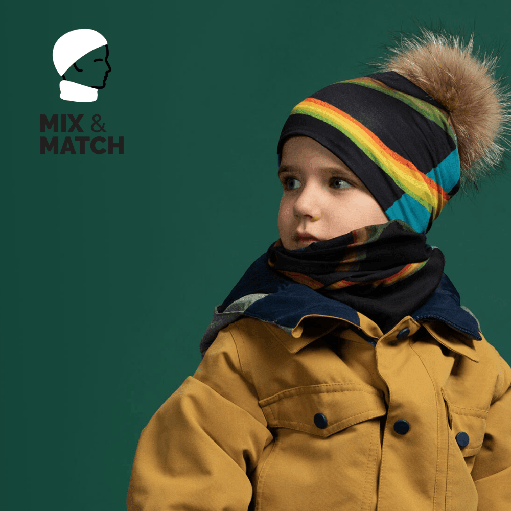 Jeune garçon portant une veste jaune et une tuque rayée colorée avec un pompon détachable en fourrure, avec un cache-cou assorti.