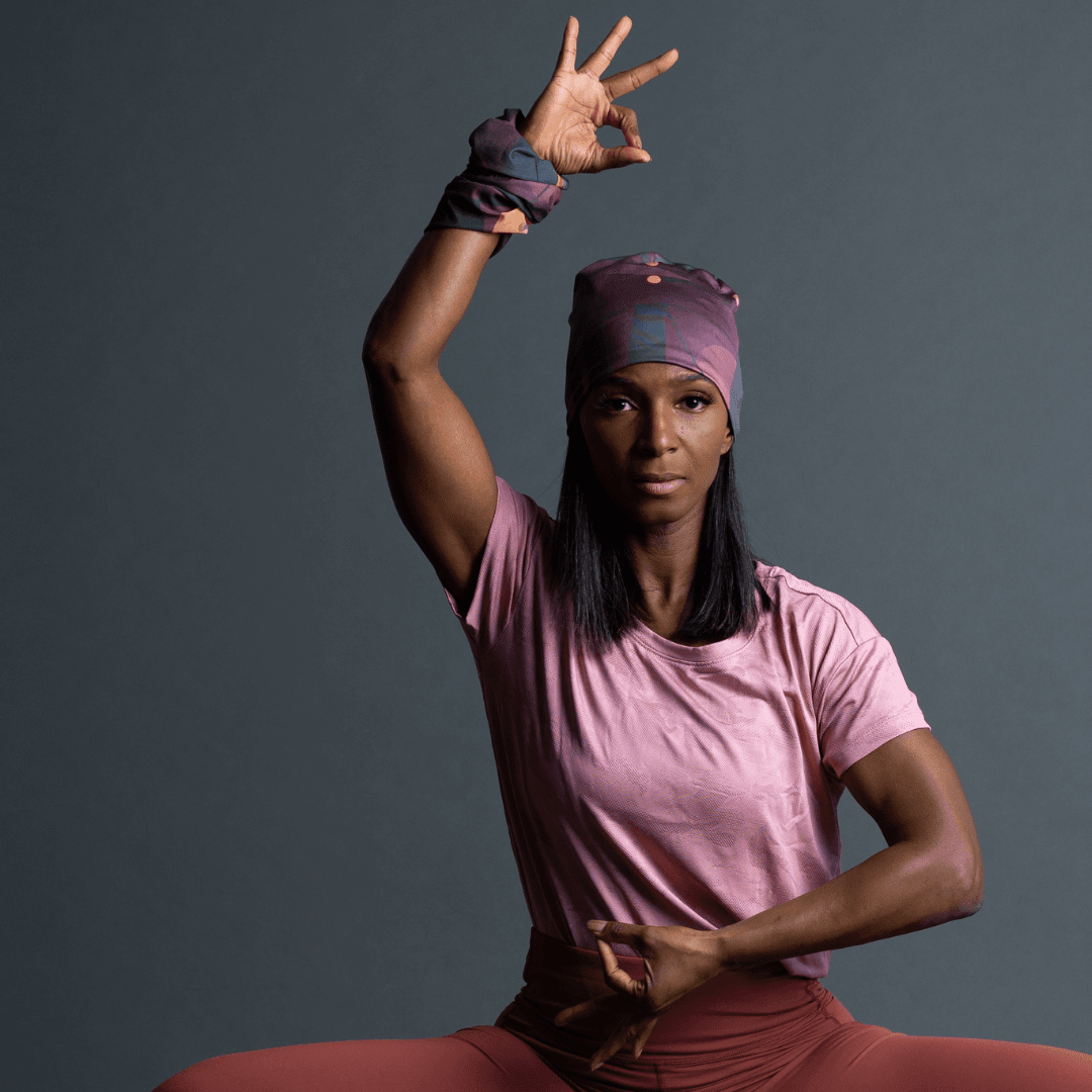 A woman in a pink t-shirt and coral leggings demonstrates wearing the purple geometric patterned bandana as a headband and wristband.