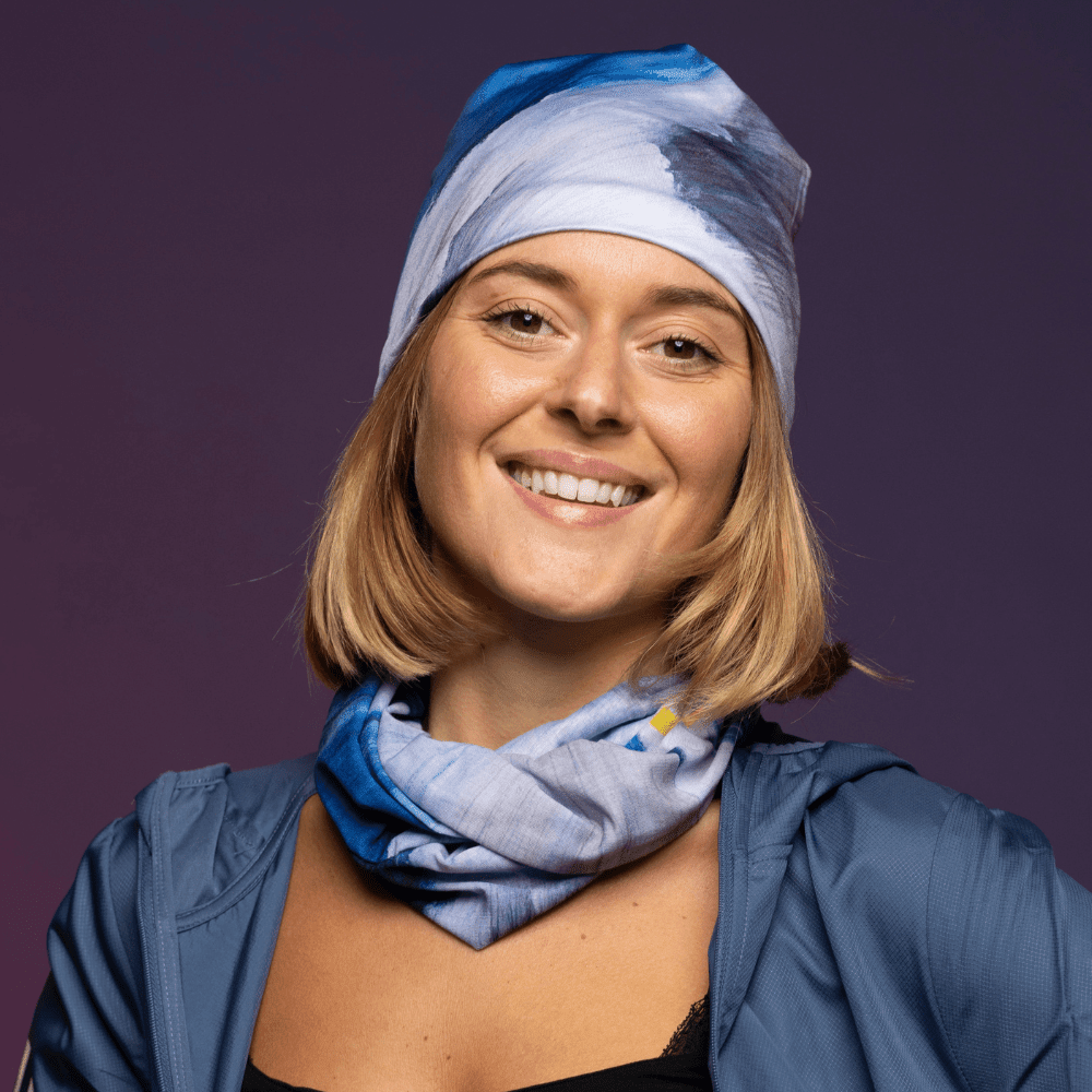 Femme souriante portant la tuque Mer Dorée et le cache-cou assorti avec une veste bleue.