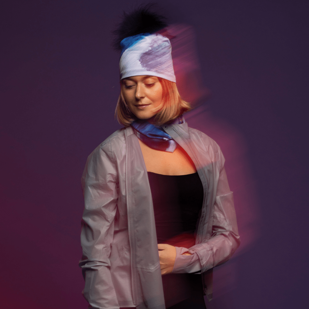 Femme portant une tuque Mer Dorée abstraite bleue et blanche et un cache-cou assorti, avec un effet de mouvement flou.