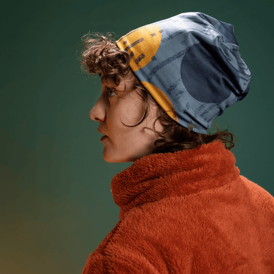 Modèle adolescent portant la tuque grise et dorée avec un manteau polaire rouille, photographié de profil sur fond vert