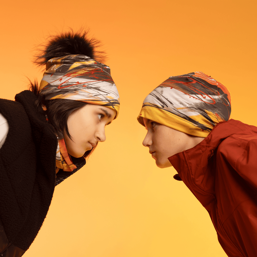 Two children wear the Le Coeur Beanies, one with a black pom-pom and the other plain, facing each other.