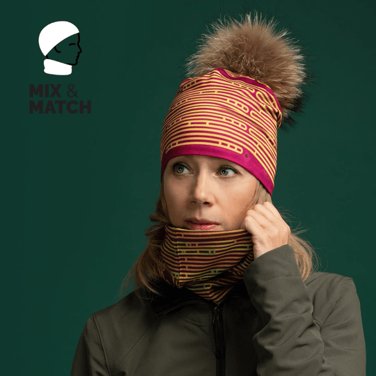 Femme portant une tuque et un cache-cou assortis magenta et jaune rayés, avec une veste verte sur fond vert foncé.