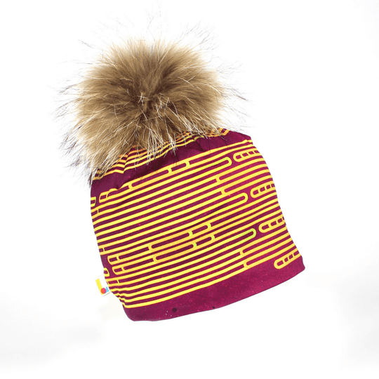 Tuque magenta et jaune rayée avec un gros pompon brun moelleux sur fond blanc.