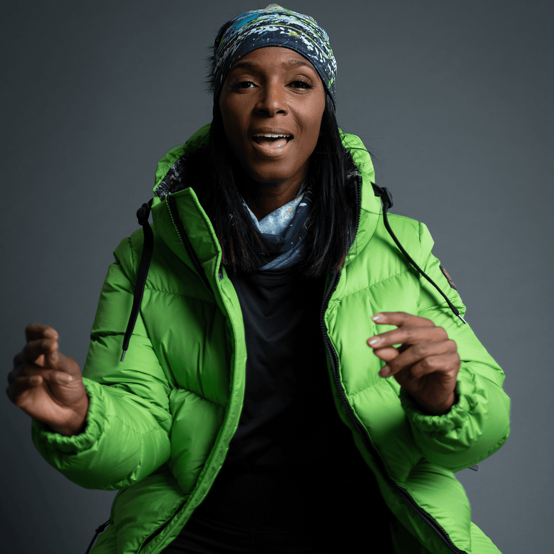 Femme portant la tuque Méduse en bandeau, souriante, dans une veste matelassée verte.