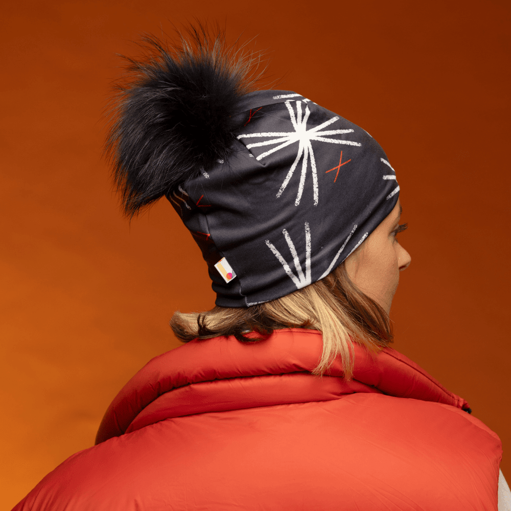 Femme portant la tuque MotifX noire avec pompon noir, vue de côté et de dos, avec un gilet rouge.