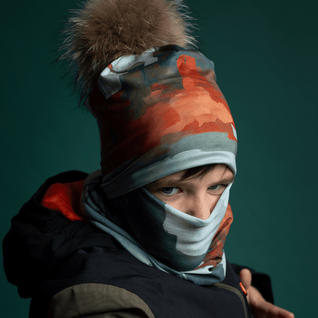 Close-up of a person wearing a colorful abstract art print neck gaiter pulled up as a face mask under a winter jacket.