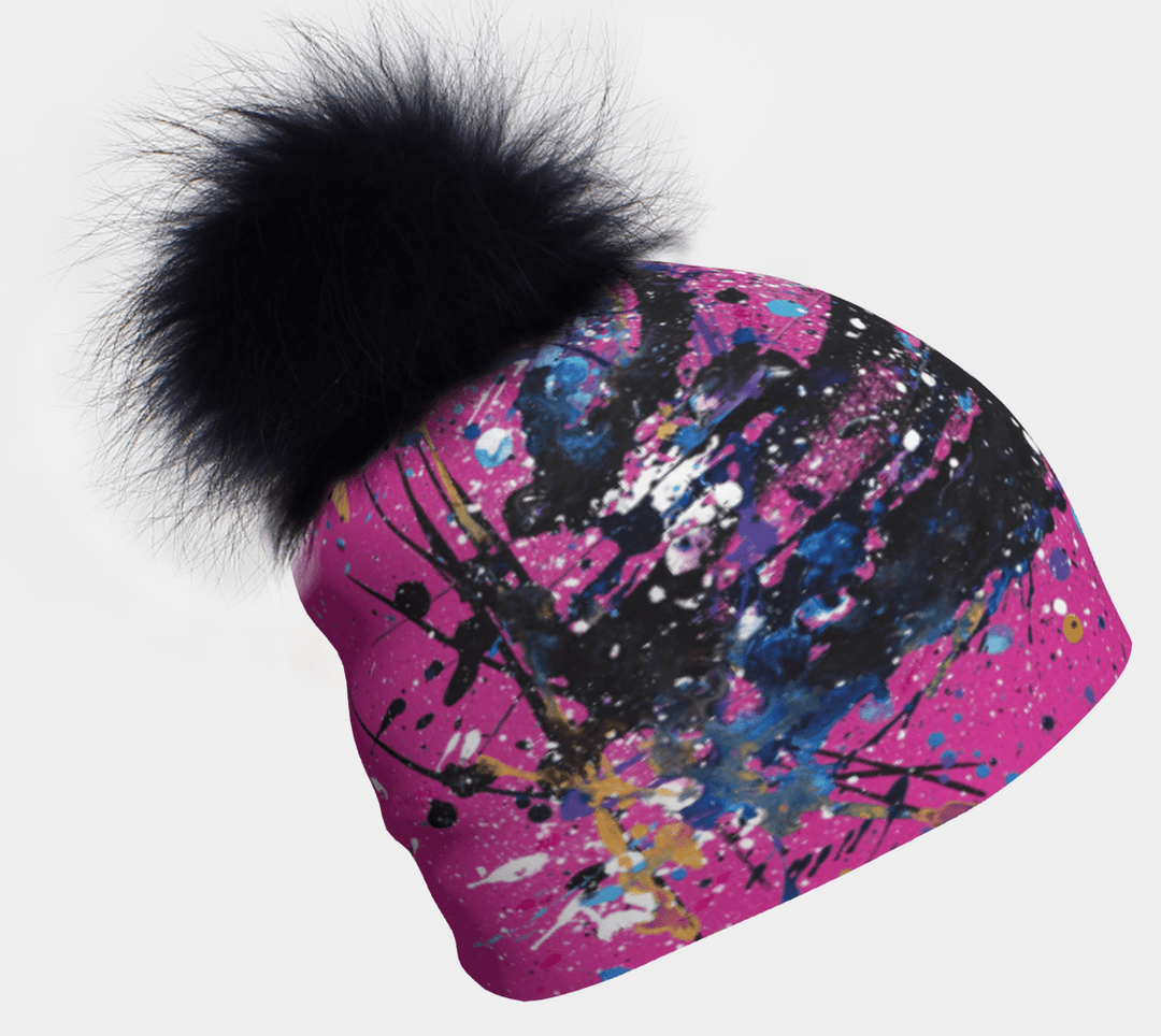 Tuque rose avec éclaboussures d'art abstrait bleu, violet, noir et jaune, surmontée d'un gros pompon noir pelucheux.