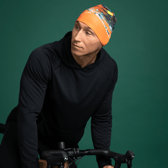 Homme portant un sweat à capuche noir et la tuque orange art abstrait, appuyé sur un vélo.