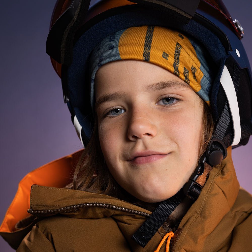 Enfant portant une tuque abstraite colorée sous un casque de ski avec lunettes et veste d&