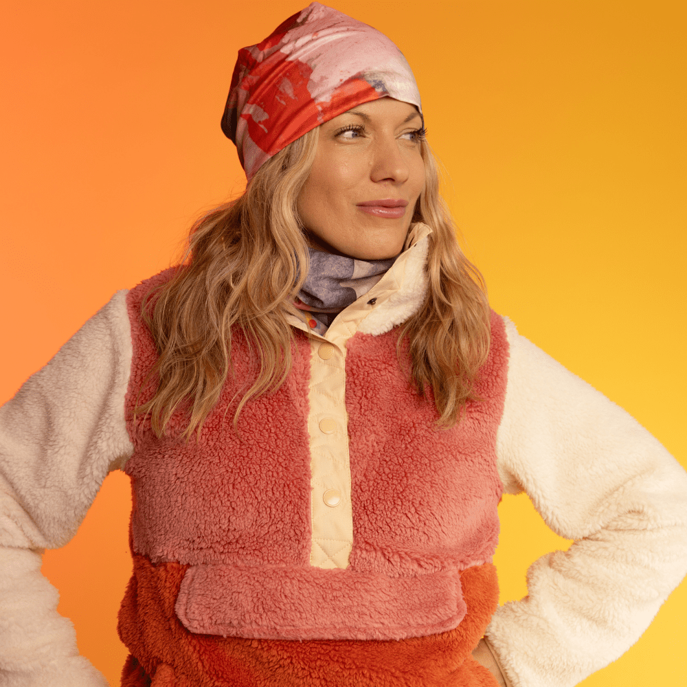 Woman wearing a beanie with abstract art and a multi-coloured neck gaiter.