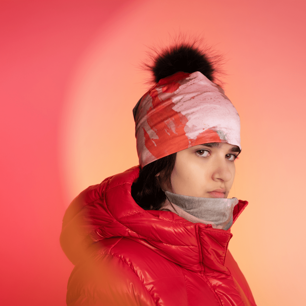 Model wearing the Pink & Flames Beanie with a black pompom and a red puffy jacket.