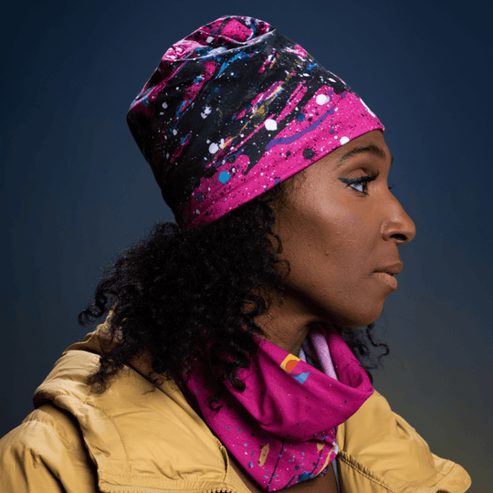 Femme portant une tuque rose à imprimé abstrait et un cache-cou assorti dans une veste jaune, profil.