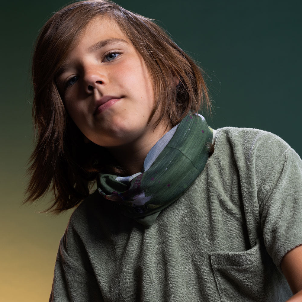 Child wearing the Amazonia multifunctional tube as a neck warmer, styled loosely over a sage green shirt