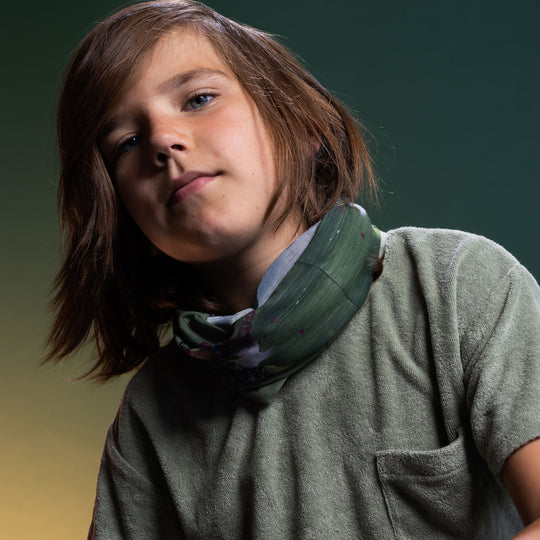 Child wearing the Amazonia multifunctional tube as a neck warmer, styled loosely over a sage green shirt