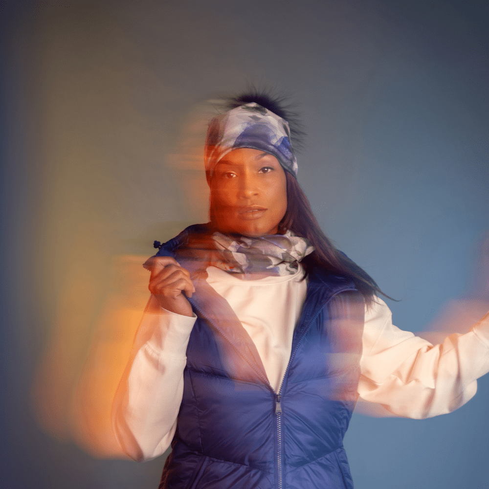 A woman wearing a blue puffer vest over a white top and a Blue Feathers patterned headband, with motion blur.