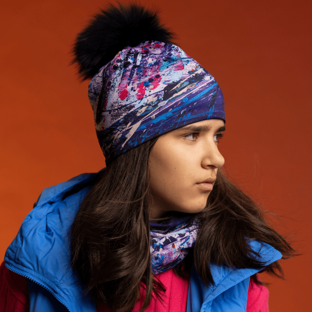 A young person wearing a blue winter jacket and a pink top, with the Cosmic beanie and neck tube from Lalita&