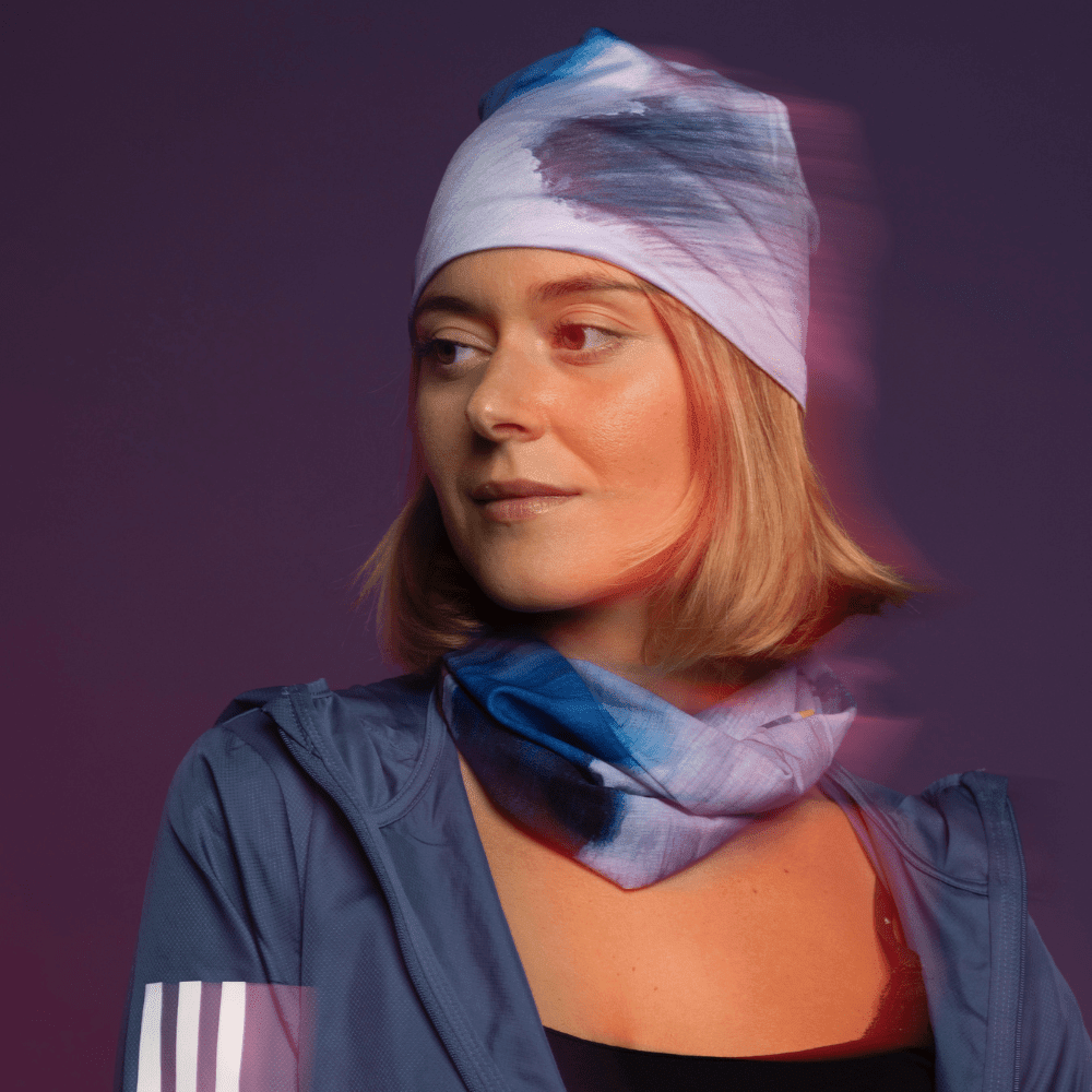 A woman wearing a blue jacket and a 'Golden Sea' printed bandana as a headband and a matching neck scarf, with a blurred effect.