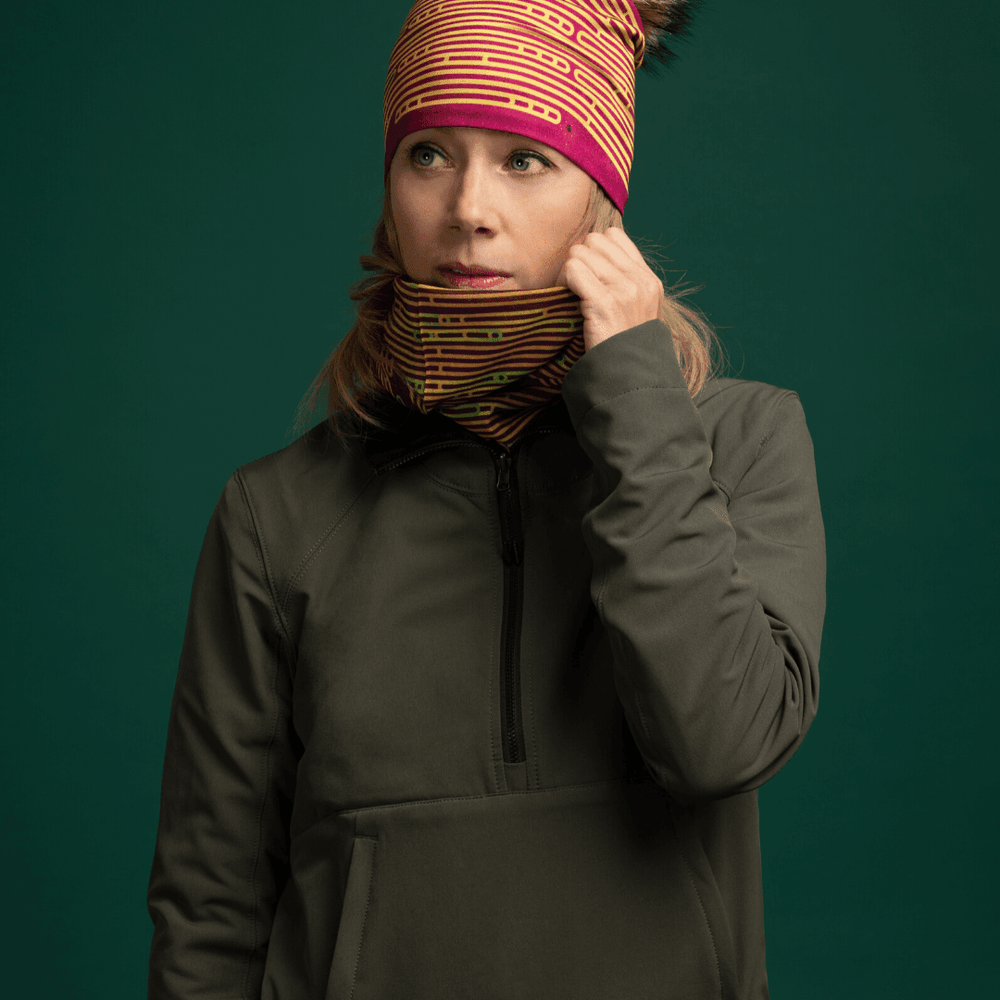 Woman wearing a green jacket and a patterned neck tube, touching the fabric near her neck.