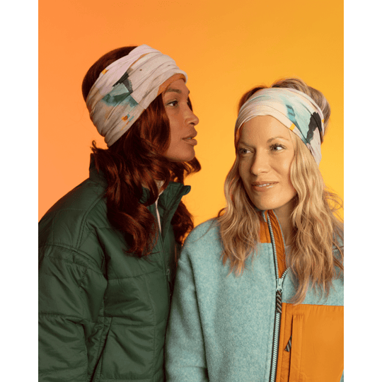 Two women wearing the POLAR Navy Accent Multifunctional Tube as headbands against a vibrant orange and yellow gradient background.