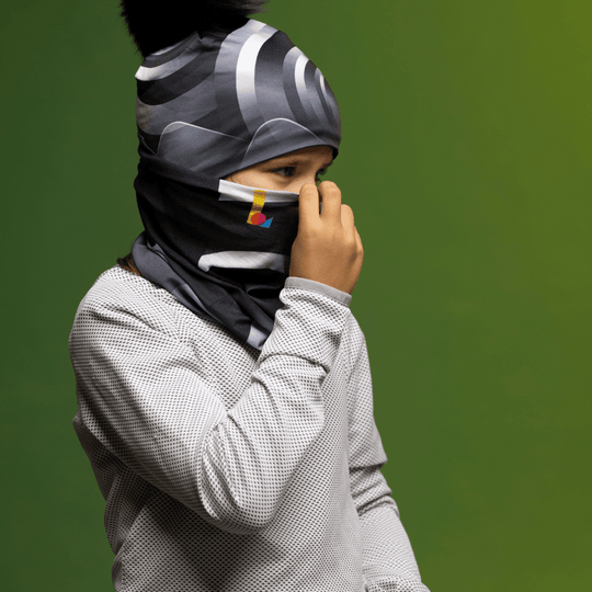 Enfant portant une chemise grise à motif gaufré et un tube de cou à imprimé abstrait noir et gris remonté comme cache-visage.