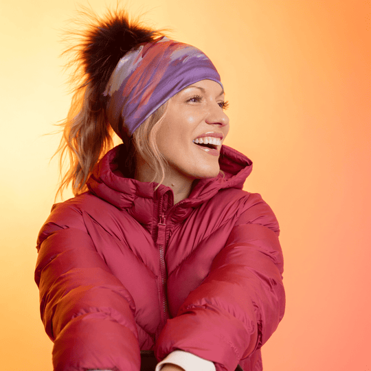 Woman wearing the Ponytail Tulips Beanie with a black pompom and a red puffer jacket, laughing.