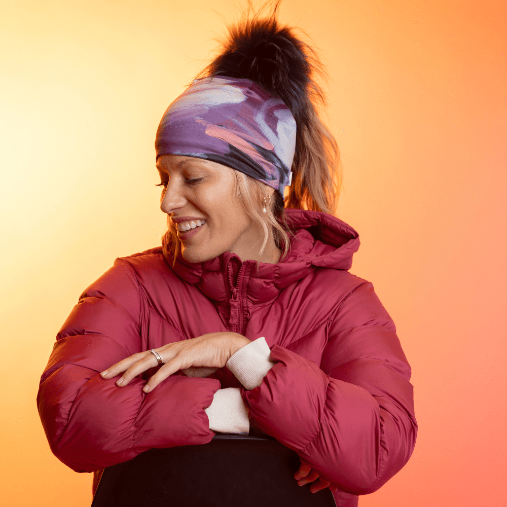 Woman wearing the Ponytail Tulips Beanie with a black pompom and a red puffer jacket, looking to the side.