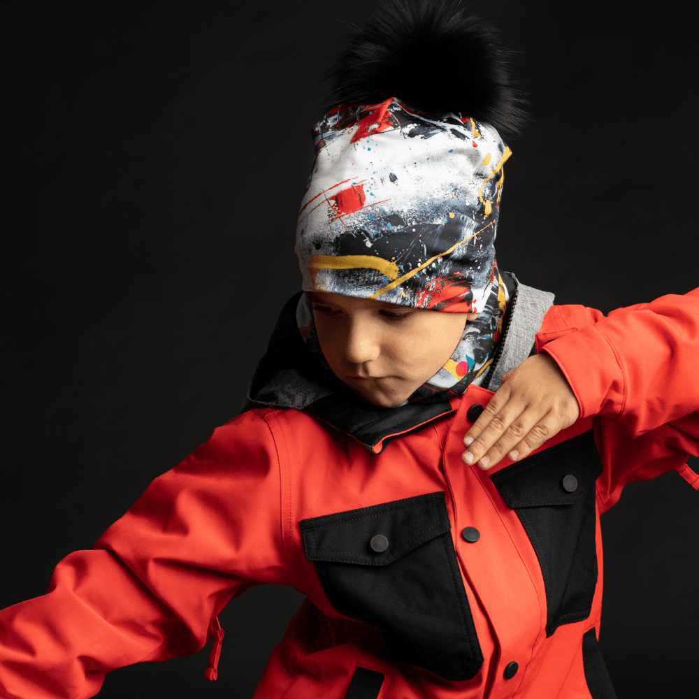 Enfant portant la tuque rouge et noire et un cache-cou assorti, sous une veste de ski rouge.