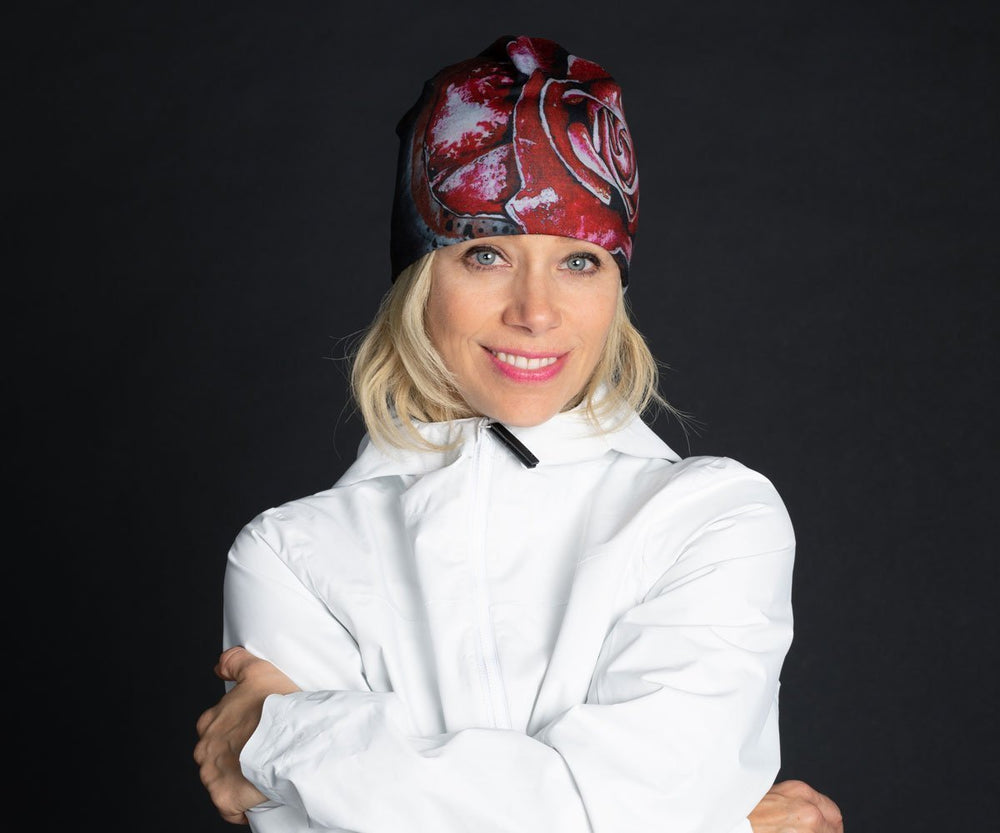 Une femme souriante portant la Tuque Rose Rouge et une veste blanche sur fond noir.