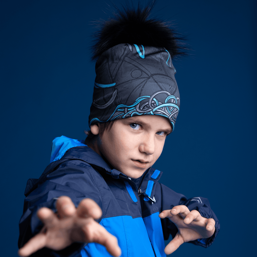 Un jeune garçon portant la tuque Robocats noire et bleue et une veste bleue, les mains tendues devant lui sur fond bleu foncé.