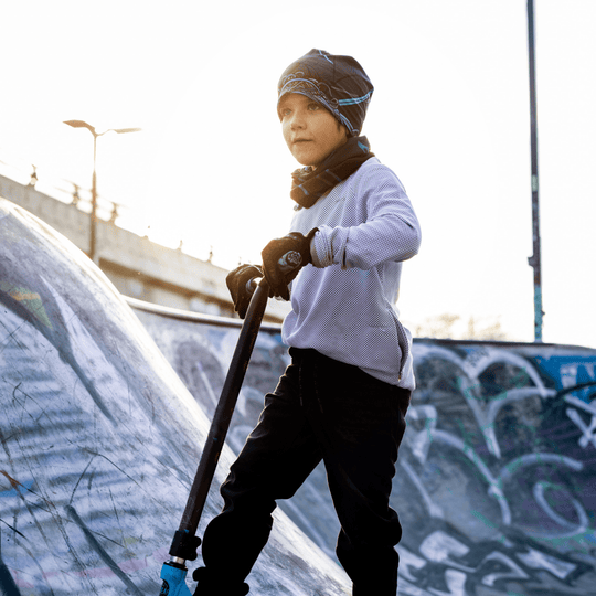 Jeune garçon avec une trottinette dans un skatepark, portant la tuque et le cache-cou Robocats.
