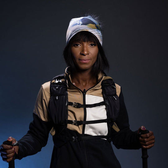 Femme portant la Tuque Sable avec Pompon Noir Amovible et un veston de randonnée, tenant des bâtons de trekking