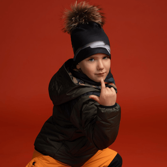 Un jeune garçon portant la Tuque Signature noire avec pompon et une veste d&