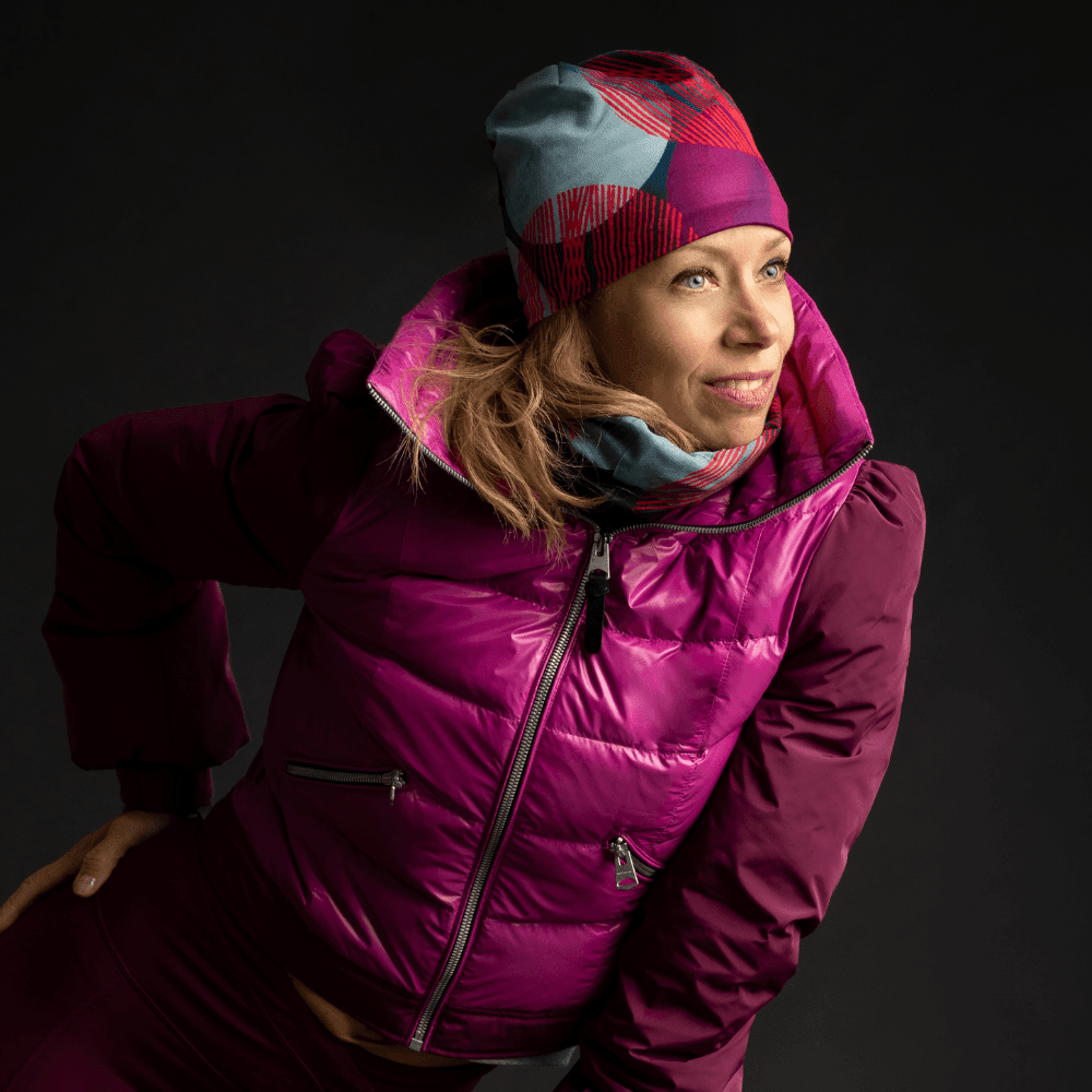 Femme en veste violette et tuque, regardant sur le côté sur fond sombre.