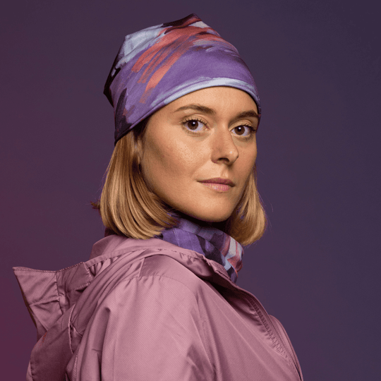 Femme portant une tuque à motif abstrait violet et un cache-cou assorti, avec une veste rose.
